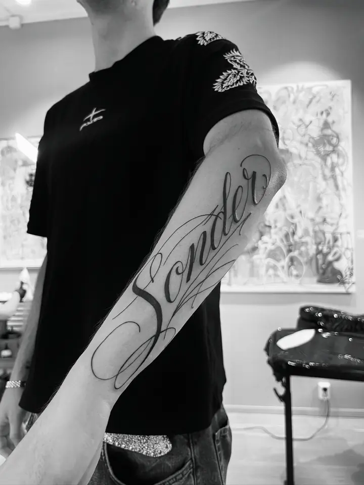 Ordet «Sonder» i skrift langs underarmen, blackwork av Abas