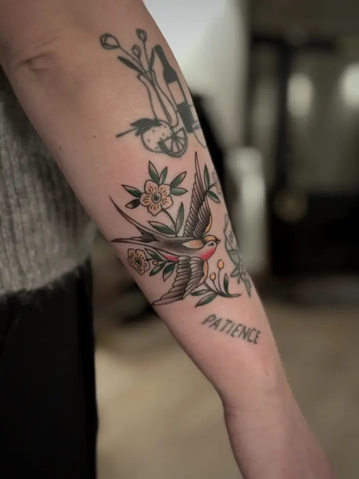 Svale, blomster og ordet «Patience» på underarmen, oldschool av Camilla