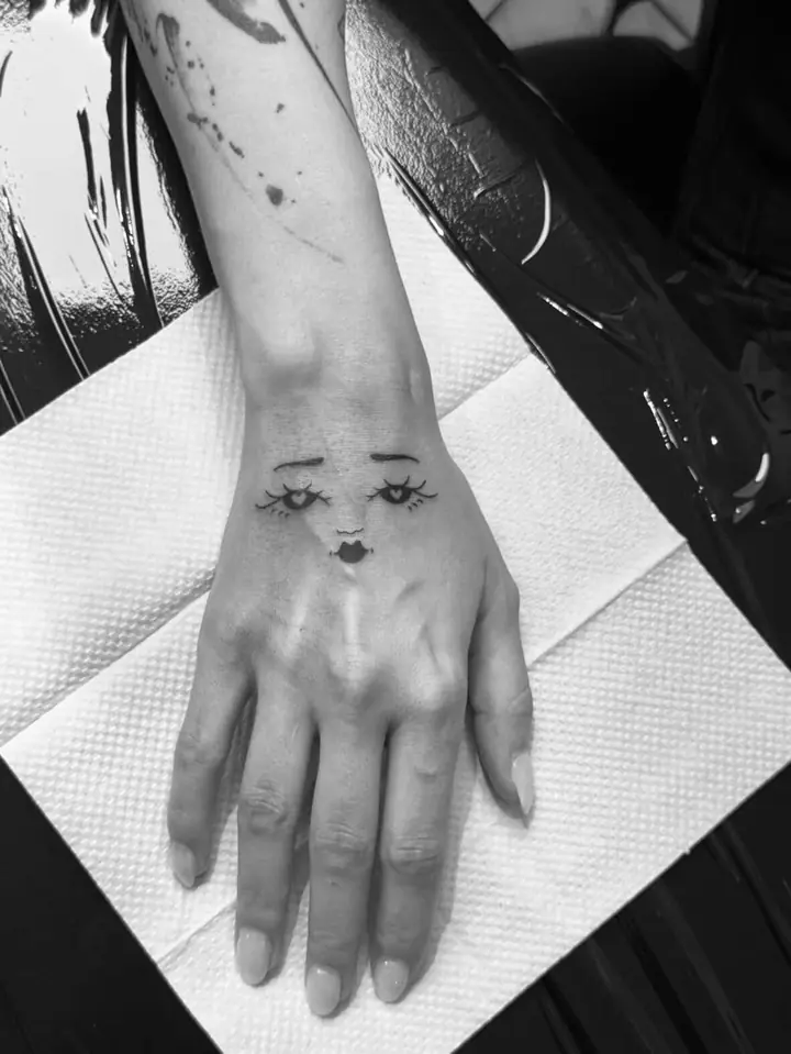 Ansikt med øyne og lepper på håndbaken, blackwork av Vilde